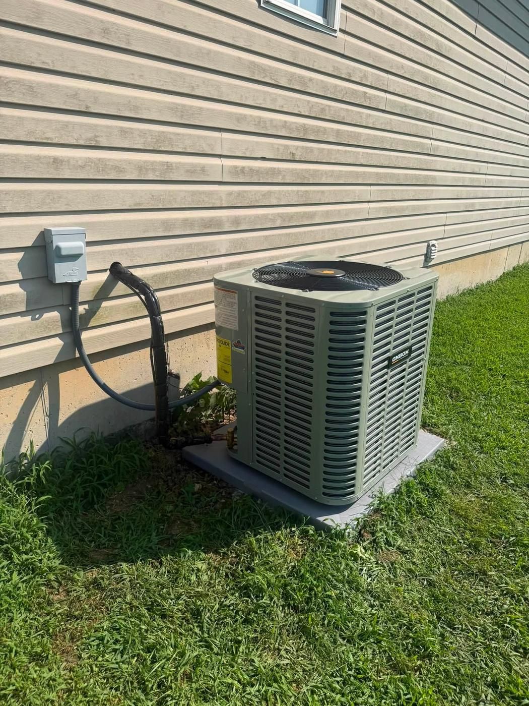 Oxbox condenser installed against tan siding with the disconnect mounted above