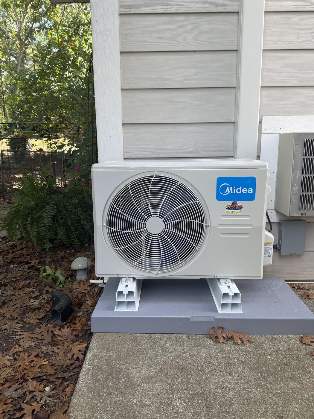 New Midea mini-split condenser installed on risers and a pad beside a house