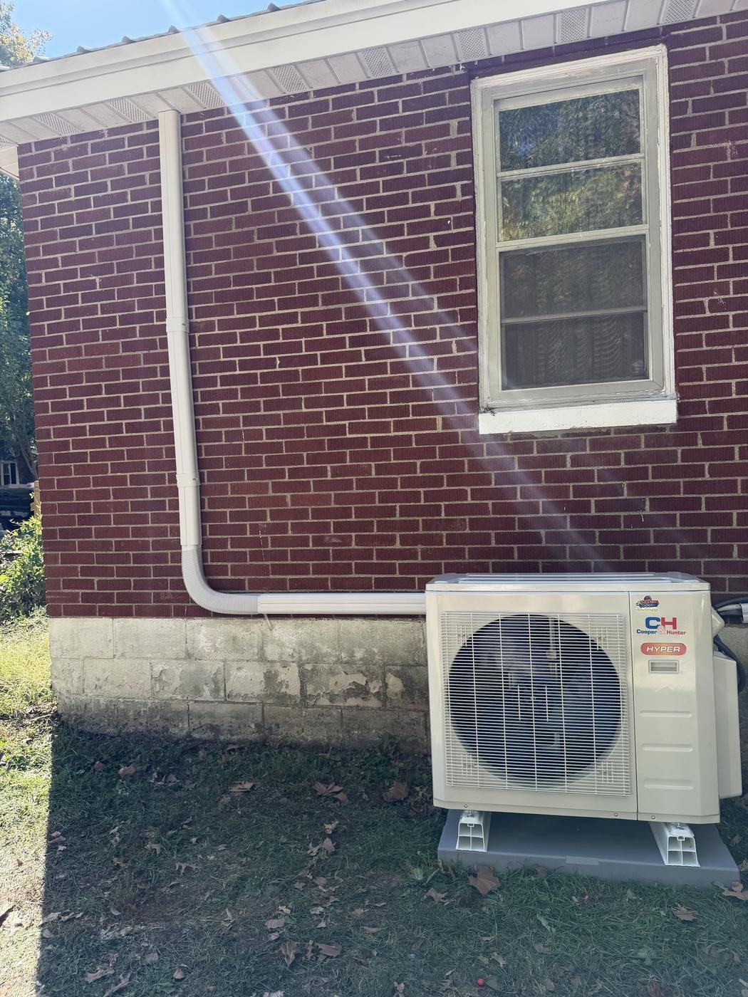 Cooper & Hunter Hyper heat pump installed on a pad against a brick wall