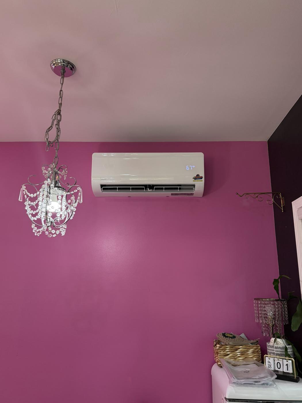 Midea mini-split indoor unit mounted high on a pink wall near a small chandelier